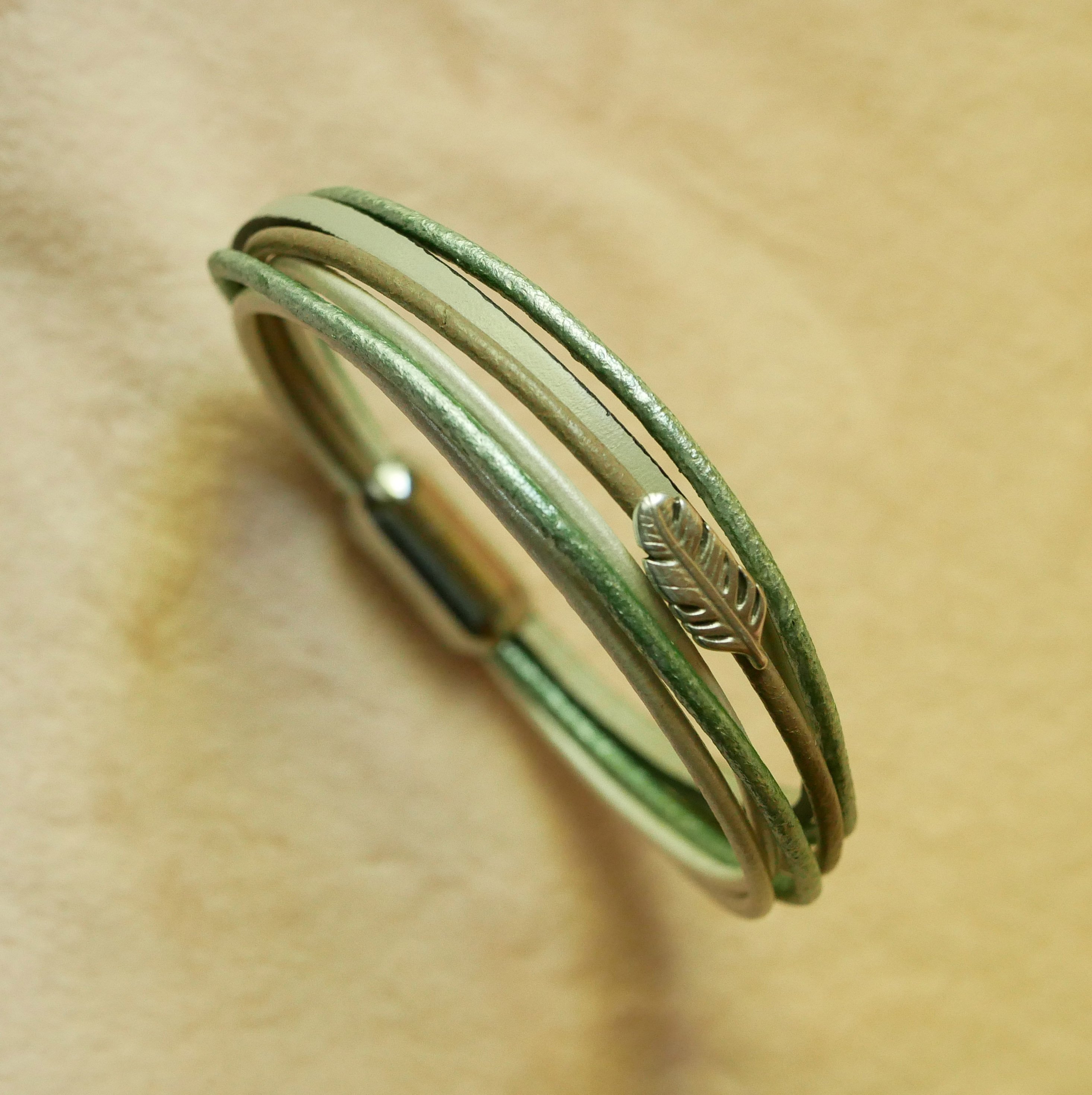 Multi-leather bracelet in shades of beige, pale green and pearly, decorated with a small feather