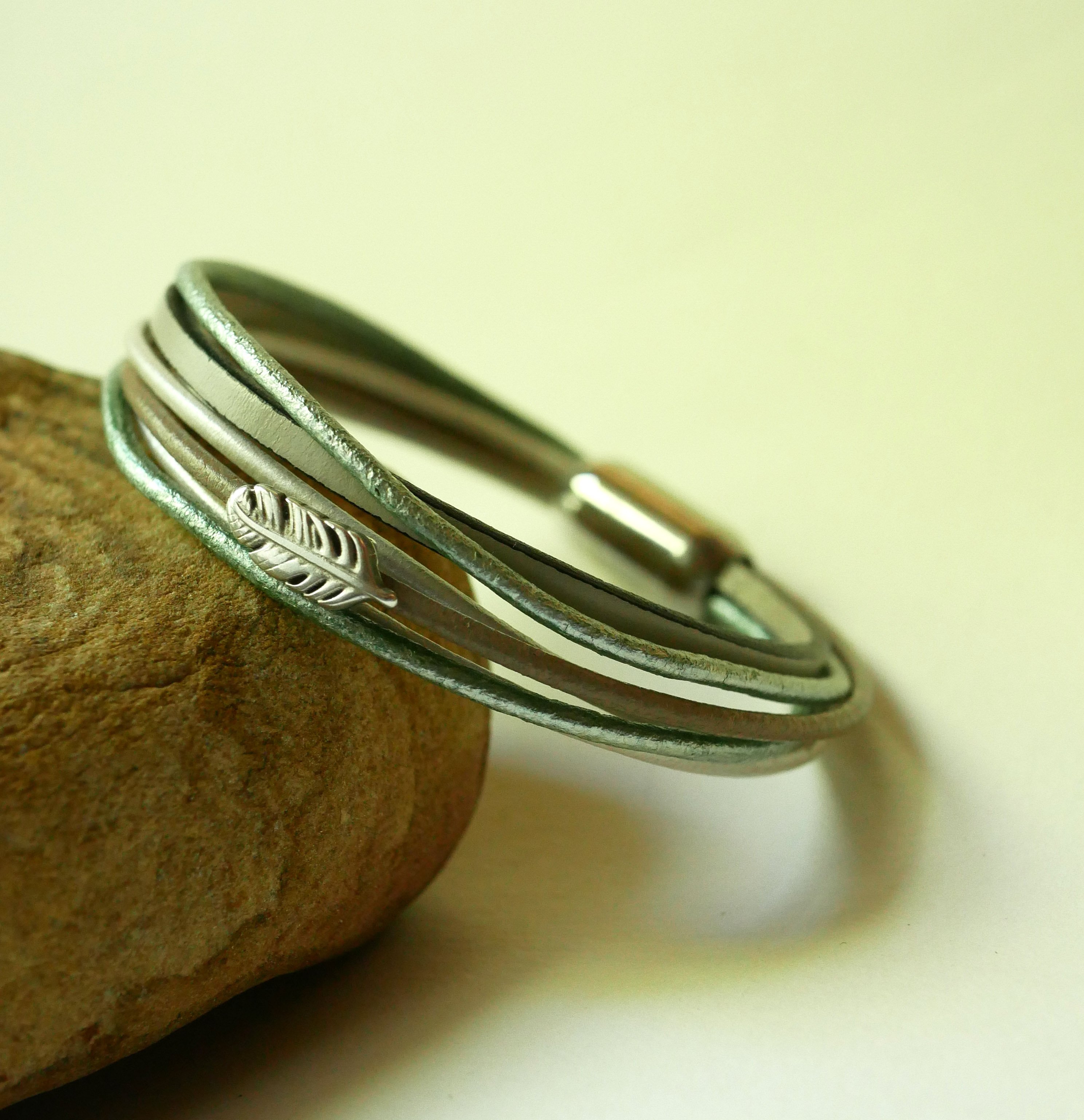 Multi-leather bracelet in shades of beige, pale green and pearly, decorated with a small feather