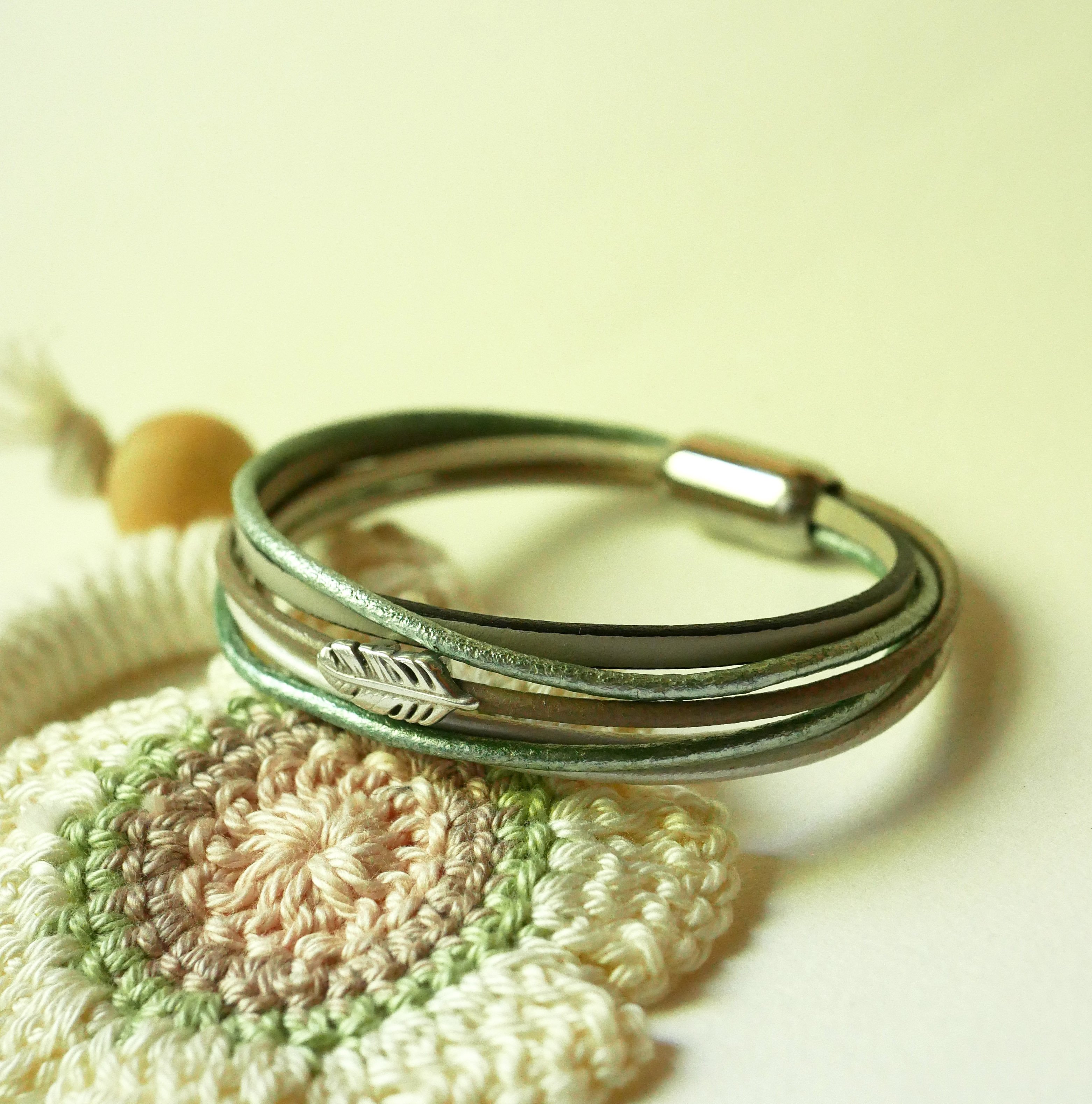 Multi-leather bracelet in shades of beige, pale green and pearly, decorated with a small feather